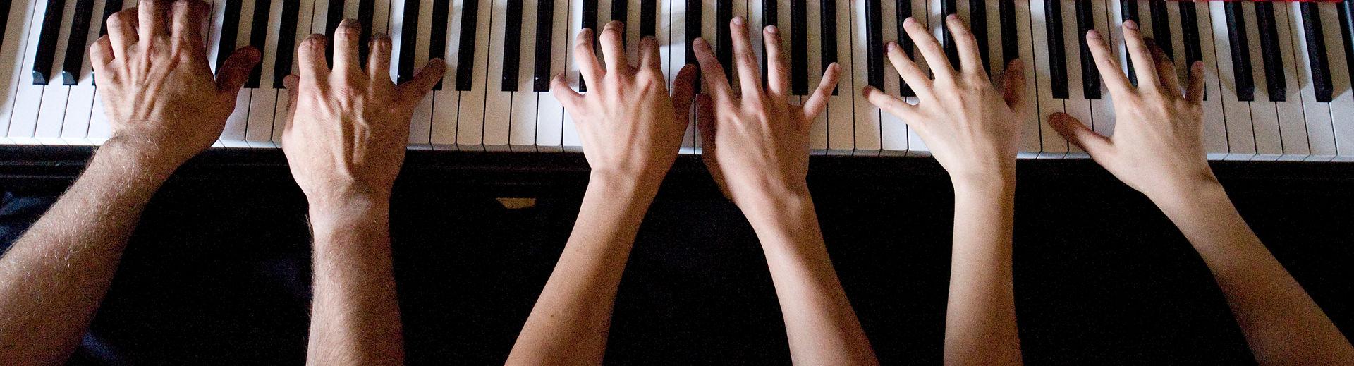 Three pairs of hands playing the piano