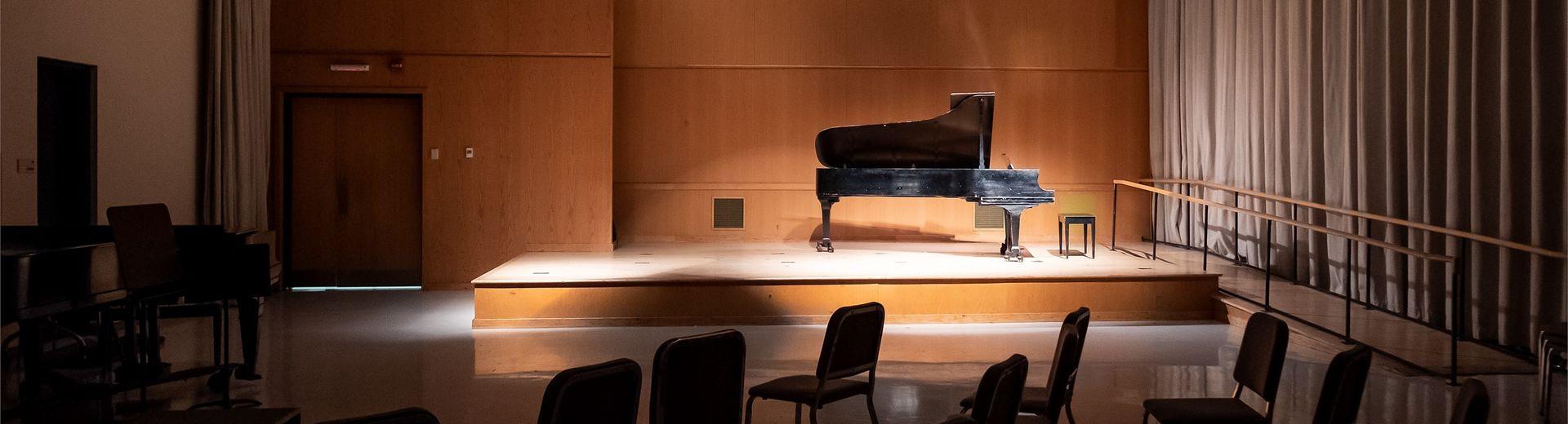 A piano sits on a stage with low lighting.